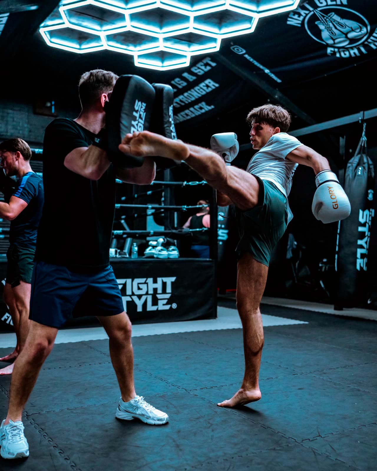 Hayden holding the kick shield for a head kick under the hexagon lights at Next Gen Fight Hub